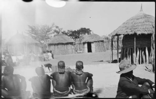 People sitting inside kraal, with huts in background