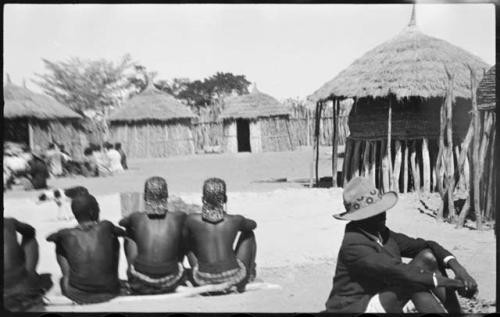 People sitting inside kraal, with huts in background