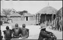 People sitting inside kraal, with huts in background