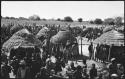 Groups of people standing, with huts in background