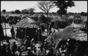 Groups of people standing, with huts in background