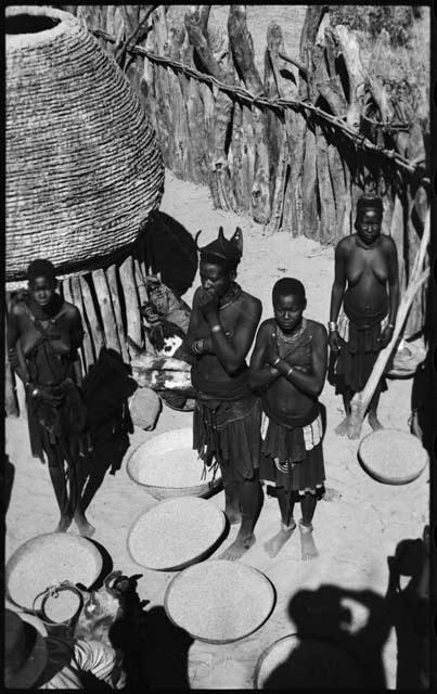 Women standing next to storage basket and baskets of grain