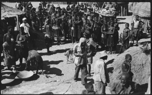 People standing next to huts, with government officials in background