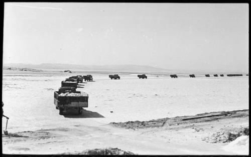 Man standing and holding a shovel, and trucks loaded with salt