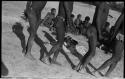 Four people dancing, with group sitting in background