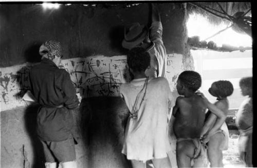 Elizabeth Marshall Thomas (taking notes) with children, inside hut