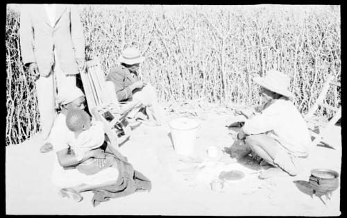 Boys, a woman (his wife), child, and two other people outside by a fire