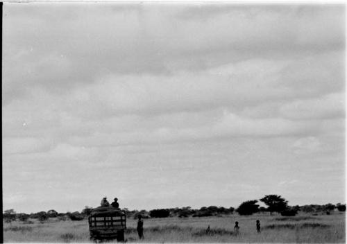 Truck in the grass with two people on top; a man and two children nearby in the grass