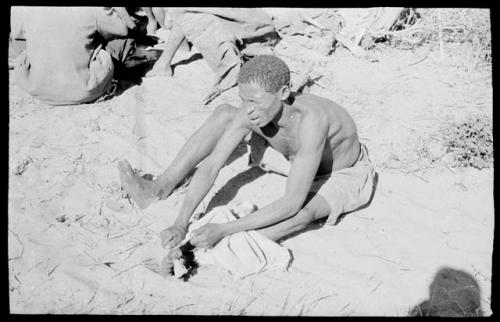 Man working on an animal skin, holding it with his foot