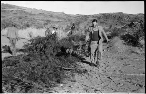 Men walking along line of brush laid out on the sand