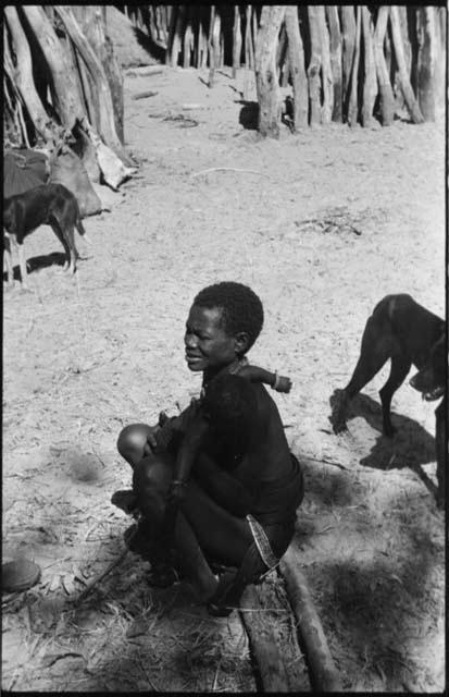 Woman sitting and holding a baby, with dogs and fence in background