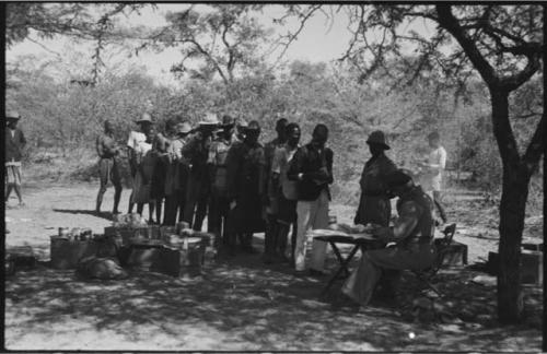 Group of men and women standing in line, possibly to pay grain tax to government official