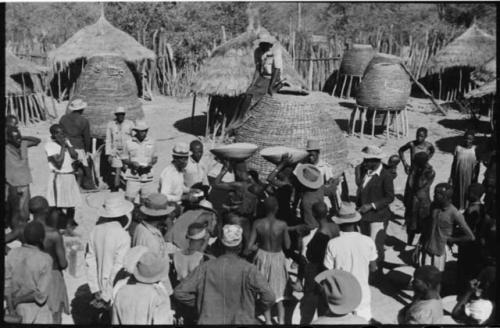 Group of people standing in front of storage baskets, and a man sitting on top of one