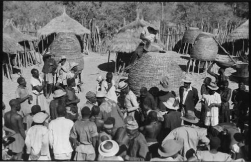 Group of people standing in front of storage baskets, and a man sitting on top of one