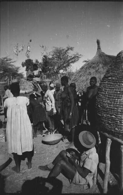 Group of people standing in front of storage basket, and man sitting on top of one and filling it with a can