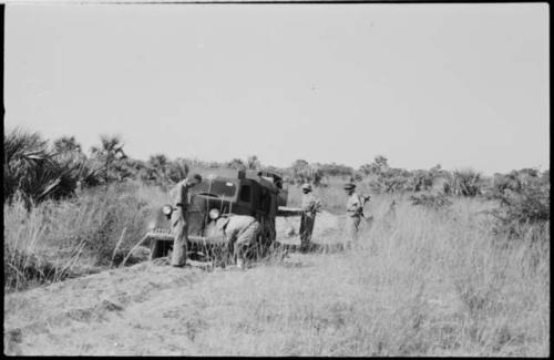 Man working on the wheel of a truck stopped on track, with three others watching