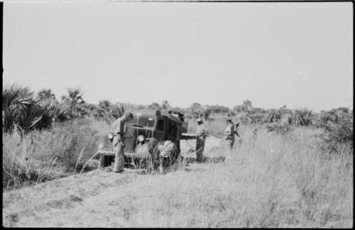 Man working on the wheel of a truck stopped on track, with three others watching