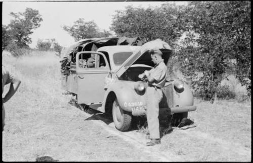 Man standing in front of a truck stopped in the track; the hood of the truck is up