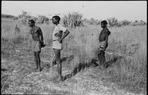 Three men standing, two of them holding bows and arrows