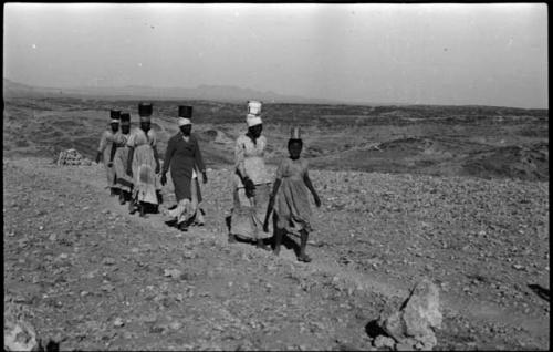 Group of people walking and carrying containers of tin ore on their heads