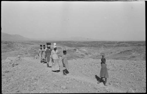 Group of people walking and carrying containers of tin ore on their heads