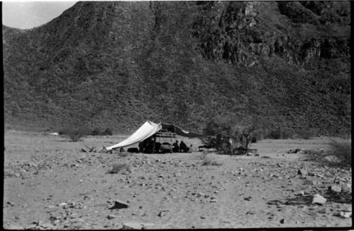 People sitting inside a tent at the foot of a hill