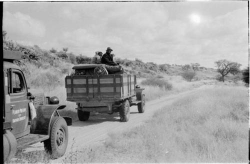 Expedition trucks on the road, two people sitting in the back of one truck