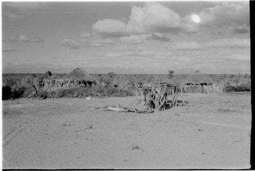 Two people standing in front of a hut, one person to the side in the clearing