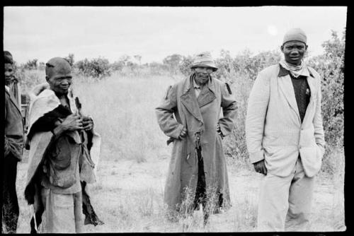 Boy in a suit, a man in an overcoat and hat, standing beside two other men