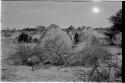 Kungwane huts in a group; two people standing amongst the huts and a group sitting in the background