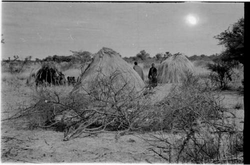 Kungwane huts in a group; two people standing amongst the huts and a group sitting in the background