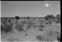 Grouping of grass huts; group of people standing on the left side