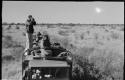 William Donnellan taking a picture on top of a truck; Simon Molamo and two other expedition members on the trucks