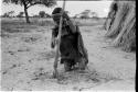 Woman on her knees digging with a hoe