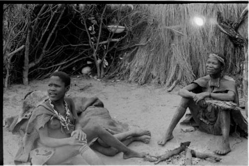 Two woman sitting and one person lying by a fire