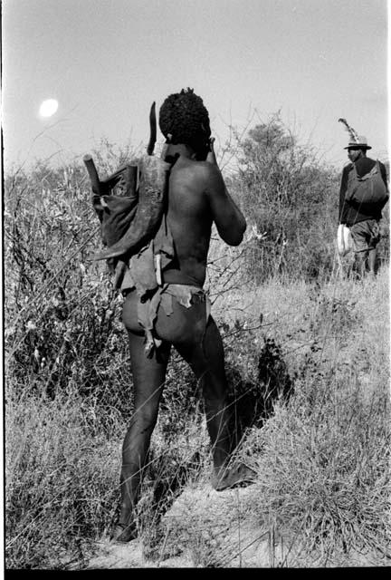 Man carrying sticks and the man wearing a hat with a feather