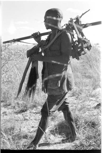 Man carrying animal traps and a gun, walking