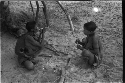 Rukan and Genitsu, with a baby on her back, sitting and lighting their pipes