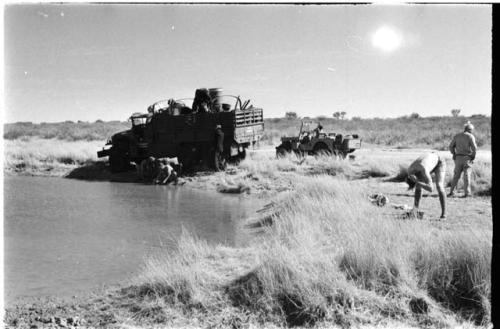 Expedition members filling barrels with water from the pan; someone bathing to the right