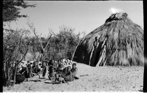 Group sitting beside a hut and a pile of tsama melons