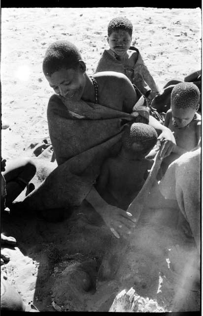 Woman sitting with three children, digging with a tire paddle