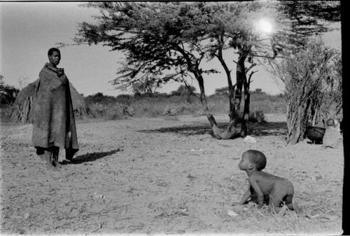 Child crawling, Mogatsiposi standing in the background wearing a kaross