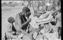 Mogatsiposi with hand to face; child sitting beside her