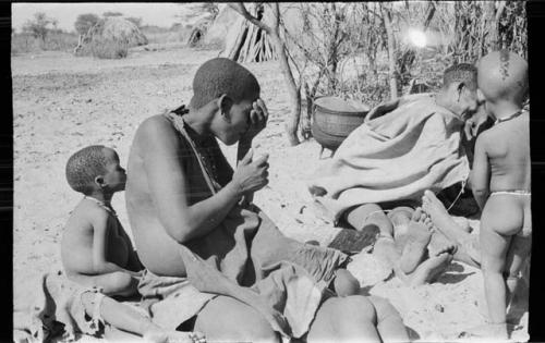 Mogatsiposi with hand to face; child sitting beside her