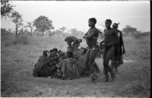 Three men, including /Gunda and ≠Gao, dancing around a group of seated women singing; medicine man leaning over "Gao Medicine" far back behind