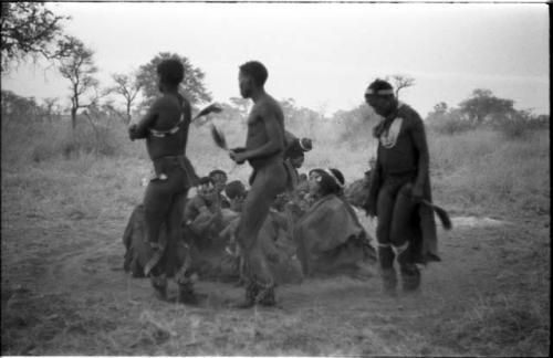 Three men, including /Gunda and ≠Gao, dancing around a group of seated women singing; medicine man leaning over "Gao Medicine" far back behind