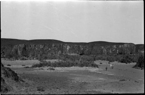 Three men walking, with cliff in background