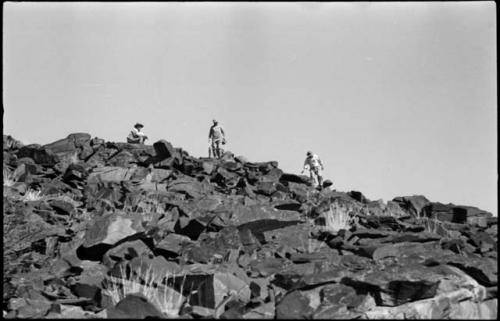 Four men standing and sitting at the top of a rocky hill