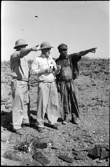 Three men standing and looking at something in the distance