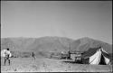 Men walking through a camp with a tent and corrugated metal shed